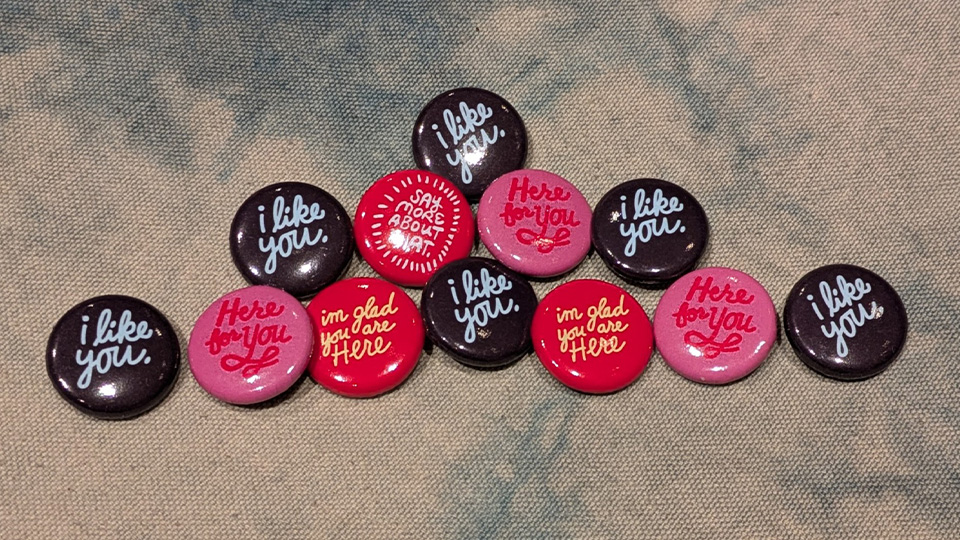 a variety of buttons with sayings on them. Sayings include 'I like you' and 'I'm glad you're here'.