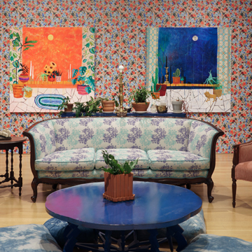 a room with a couch, coffee table and paintings on a wallpapered wall