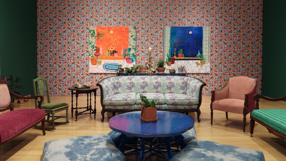 a room with a couch, coffee table and paintings on a wallpapered wall