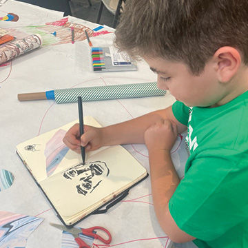 a young boy draws a portrait in a sketchbook