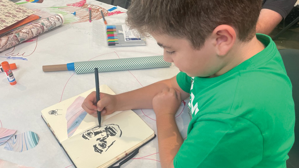 a young boy draws a portrait in a sketchbook