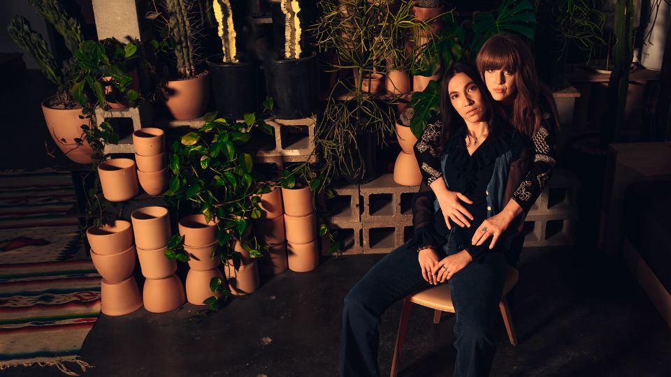 two women - one is sitting in a chair and the other stands behind with arms around her