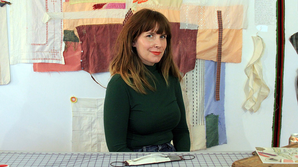 Hadley Clark sitting in front of a mended blanked that is hanging on the wall behind her