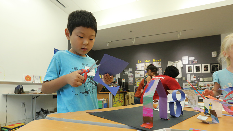 a young boy cutting a piece of construction paper during a Saturday workshop