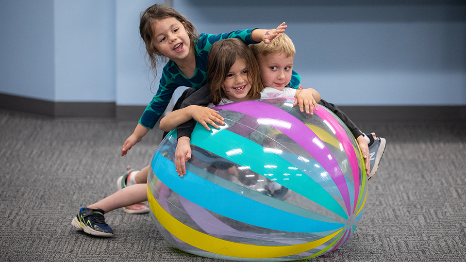 three small children playing with a large inflatable ball