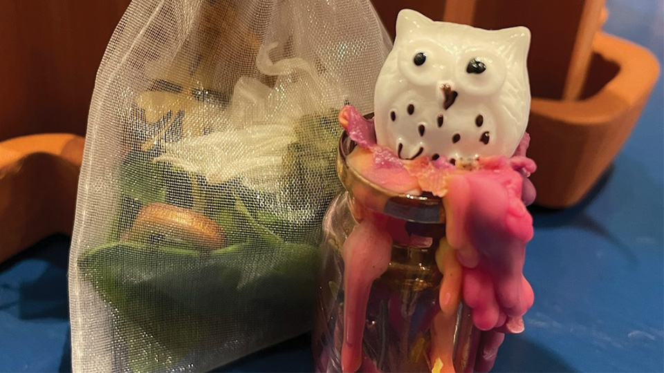 an owl figurine sitting on melted glass on top of a bottle and a satchel for potpourri
