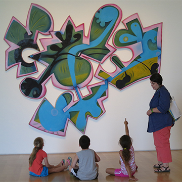 3 children sitting on the floor in front of a large work of art in the Nerman while an instructor talks about the piece