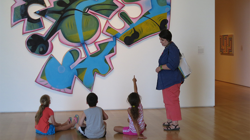 3 children learn about a work of art in the Nerman Museum from a female instructor