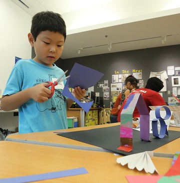 a young boy cutting a piece of blue construction paper