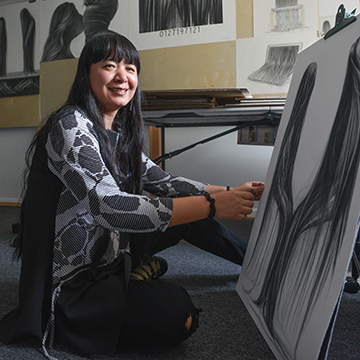 Hong Chun Zhang in her home studio. She is sitting on the floor next to a canvas she is working on.
