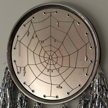 Tin Milagros, chain, woven silver web, charms, grommets and silver tassels attached to lowrider hoop