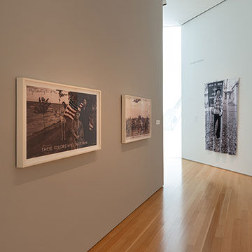 exhibition view showing three photographs and a colorful mixed media work in the shape of a shield
