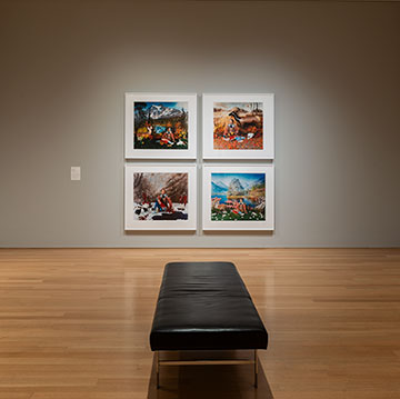 wide view of the PhotograpHER exhibition at the Nerman Museum showing three of the gallery walls displaying four works of art and a bench in the center of the room