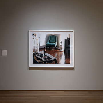 A photo of an empty room with a blue chair is displayed in a gallery at the Nerman for the PhotograpHER exhibition
