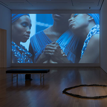 Closeup of three women wearing blue garments who are embracing and holding hands with their eyes closed.