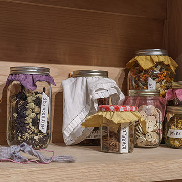 8 canning jars on a shelf containing various seeds and buttons.