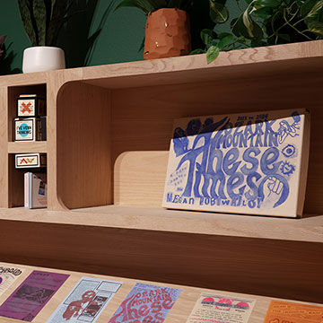Items displayed on a wooden bookshelf including games, signs and graphic design prints.