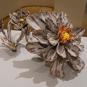 A ceramic sculpture of a multi-petaled flower blossom and vine in muted colors.