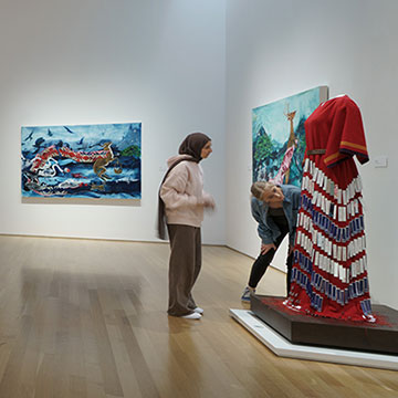 museum visitors look closely at a dress created by Julie Buffalohead