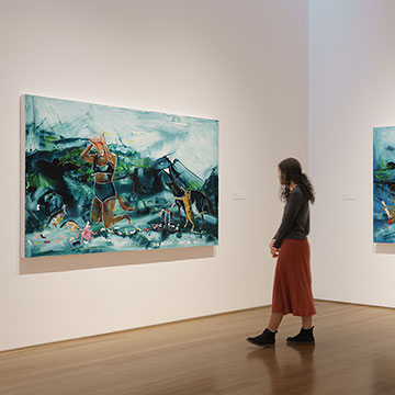 a museum guest walks in between two large paintings by Julie Buffalohead on display at the Nerman Museum in Overland Park, KS