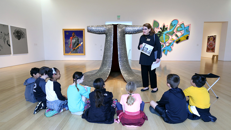 A volunteer docent talks to a group of children sitting crosslegged around a sculpture at the Nerman
