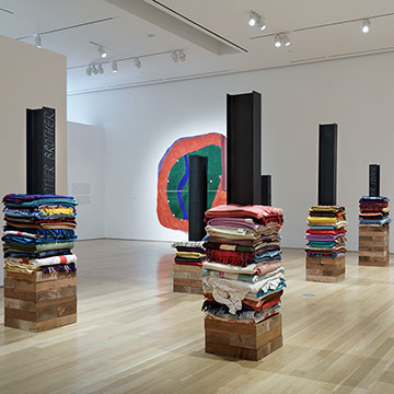 installation by Marie Watt and Teresa Baker of folded blankets sitting on top of cedar boxes with iron I-beams on top of them