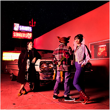 Three women in a parking lot in a color photograph by Cara Romero.